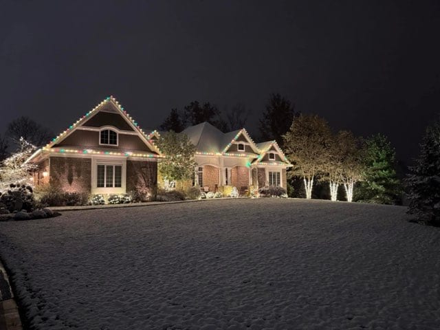 Wide estate frontage lit across several gables with trees picked out along the driveway