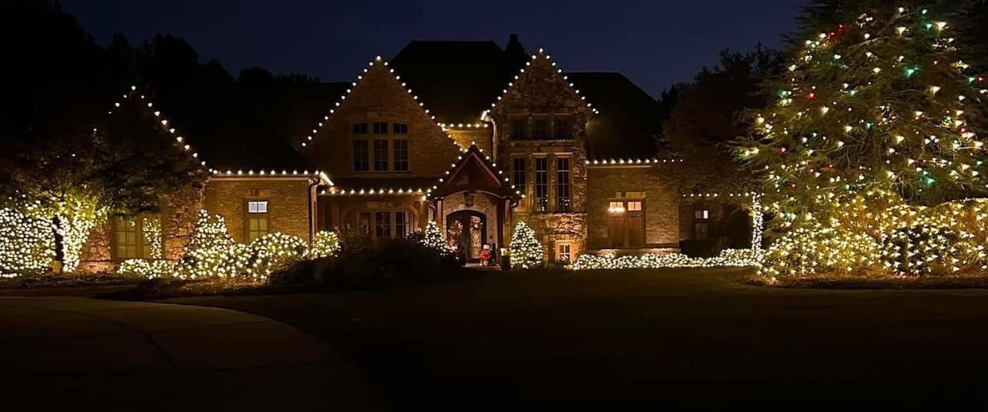 Wide estate frontage outlined in warm white with wrapped shrubs and a lit tree