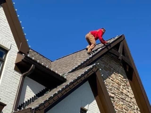 Mike’s Outdoor Services installer clipping lights along a roof edge against a clear sky