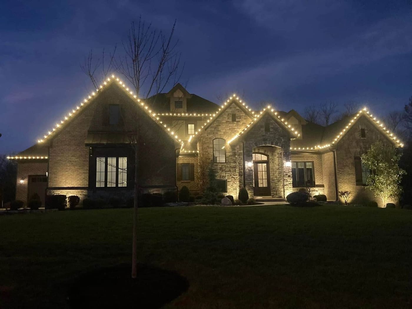 Every gable and peak picked out in warm white on a stone and brick home
