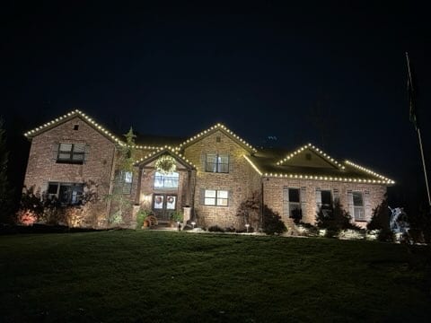 Stone and brick home with warm white lights along every roofline