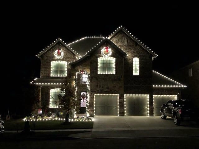 Two storey brick home with lit wreaths in the upper windows and every garage bay outlined